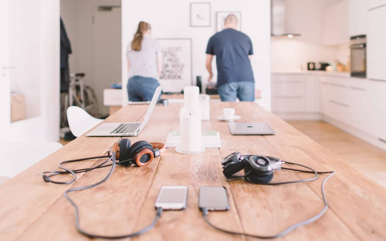 Two people working at a long table at home with laptops and phones, the kind of setup where shared Google documents get printed
