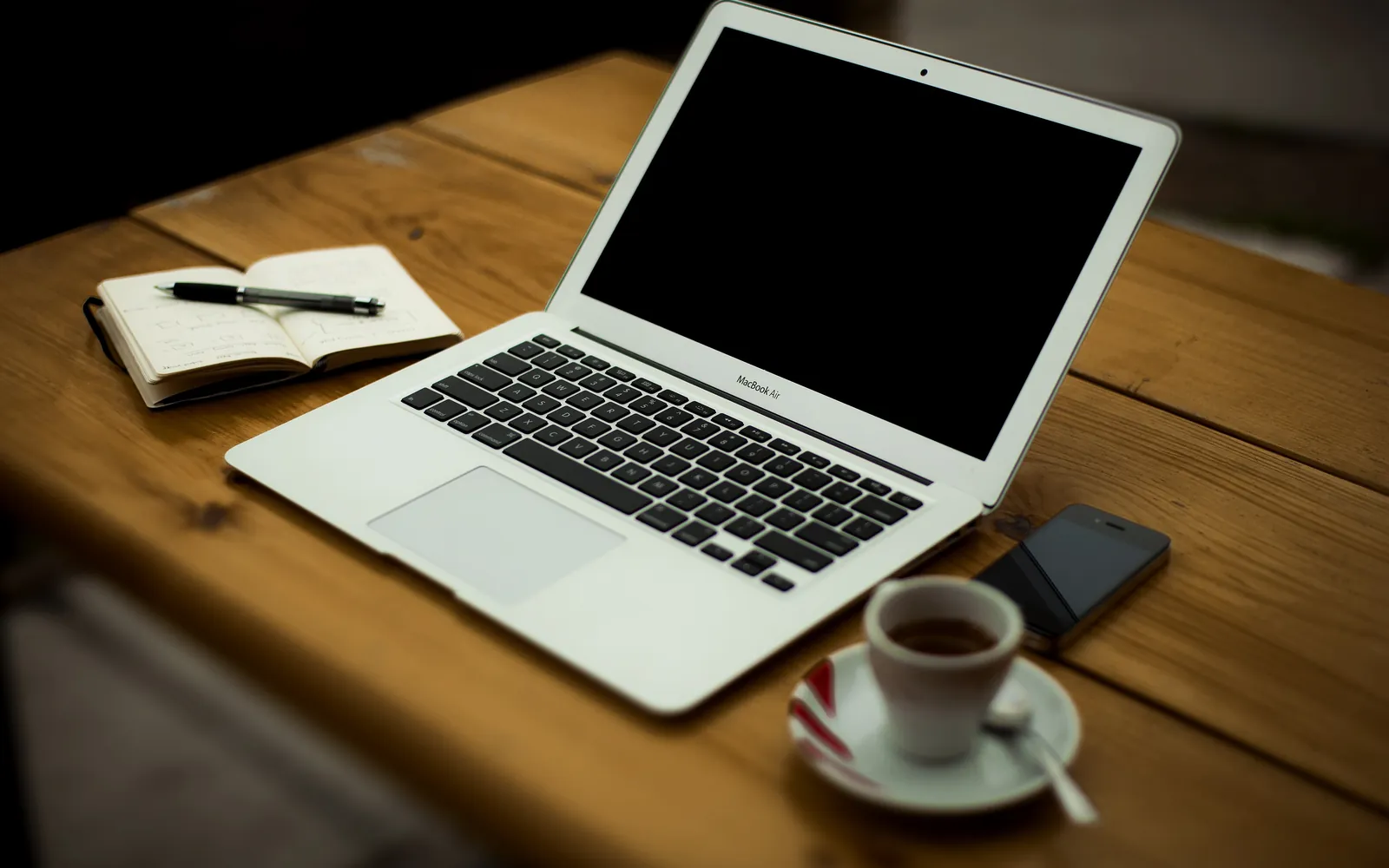A laptop, notebook and coffee cup on a wooden desk at home