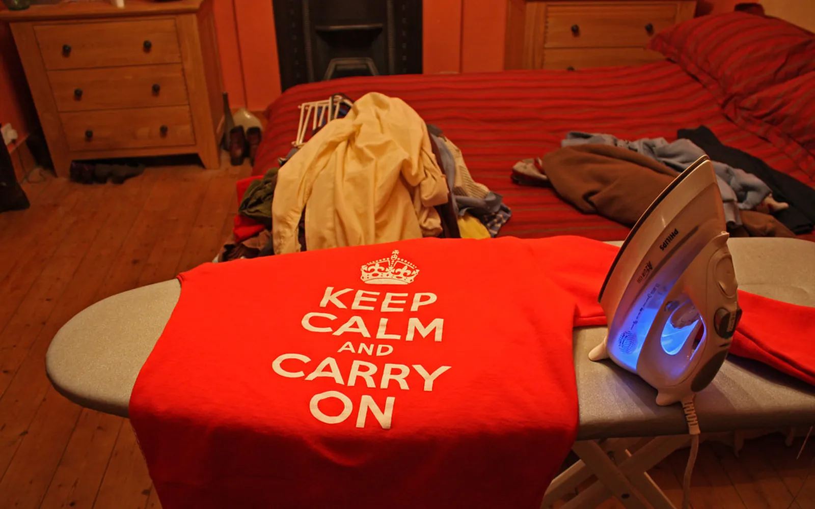 A steam iron resting on a red printed t-shirt laid over an ironing board